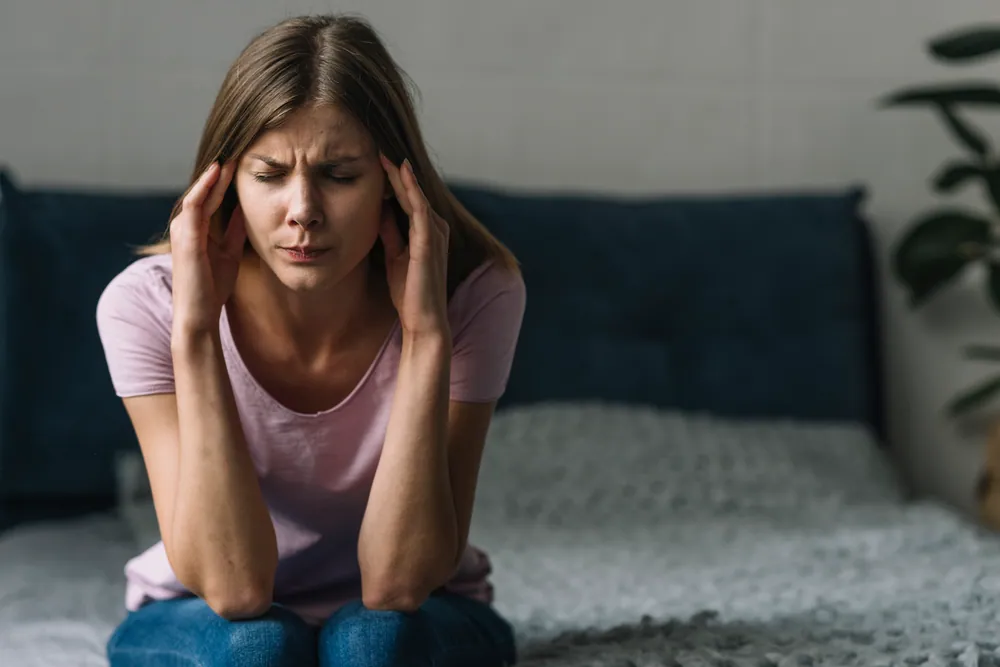 blonde woman holding her head due to migraine pain