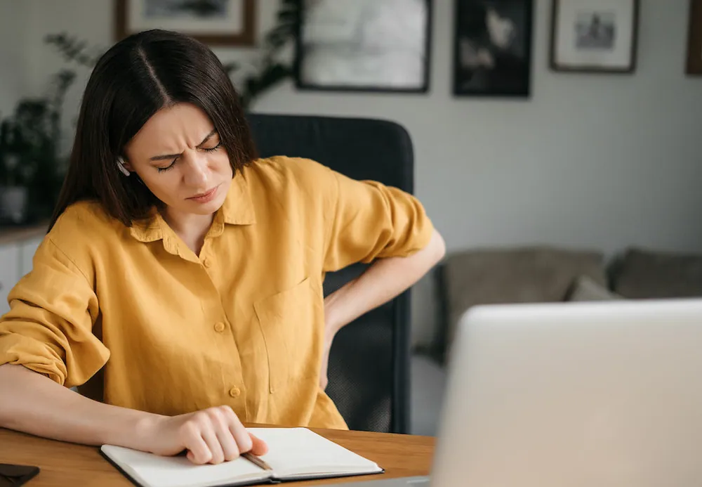 woman wearing yellow top in pain due to poor posture sitting